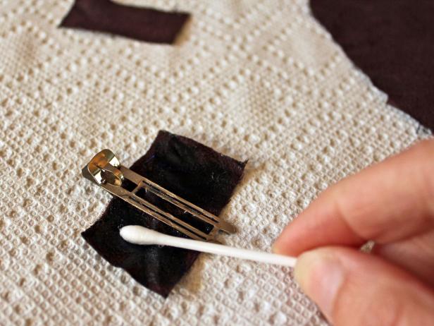 Cut a piece of fabric that's a bit smaller than the large leather circle previously cut for the pin. Slide fabric through clip or pin back, than apply adhesive to fabric and the side of the metal that will be in contact with leather.