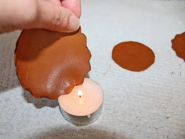 Light a votive or taper candle. Using caution, hold a leather circle over the flame — but do not let the leather come in direct contact with fire — until the edge begins to curl, then rotate the leather to expose a new area to the heat.