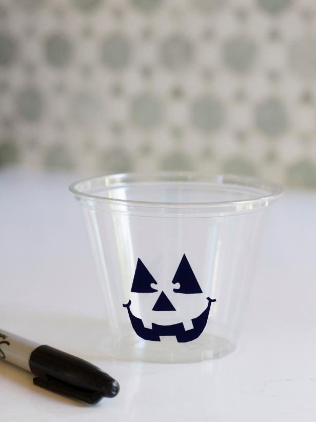 Use a black permanent marker to draw a sinister, sad or happy jack-o'-lantern face onto the front of each punch cup.