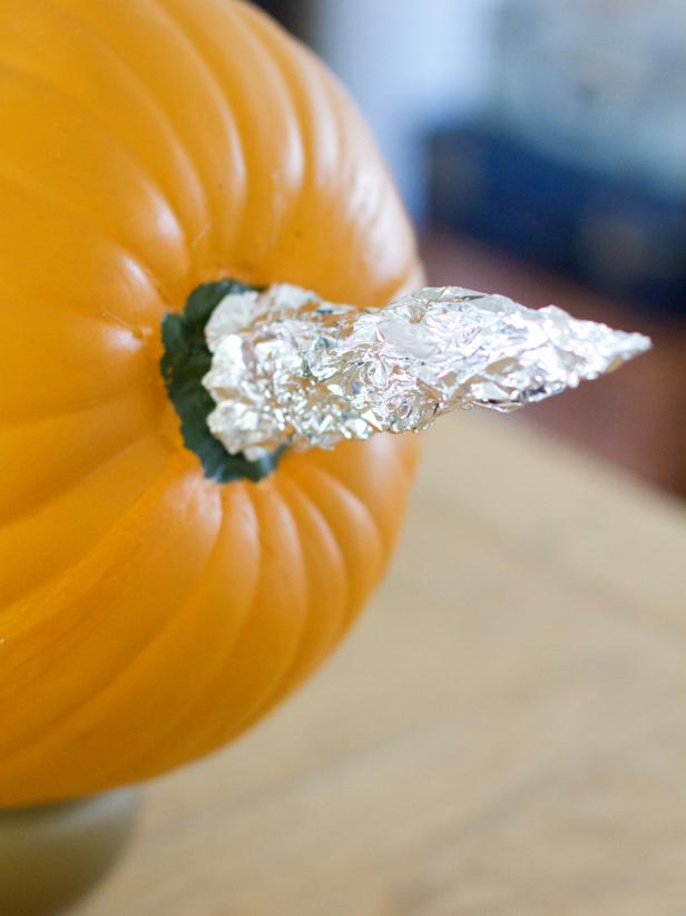 Twist a piece of aluminum foil into a cone shape then attach it to the pumpkin's stem with hot glue.