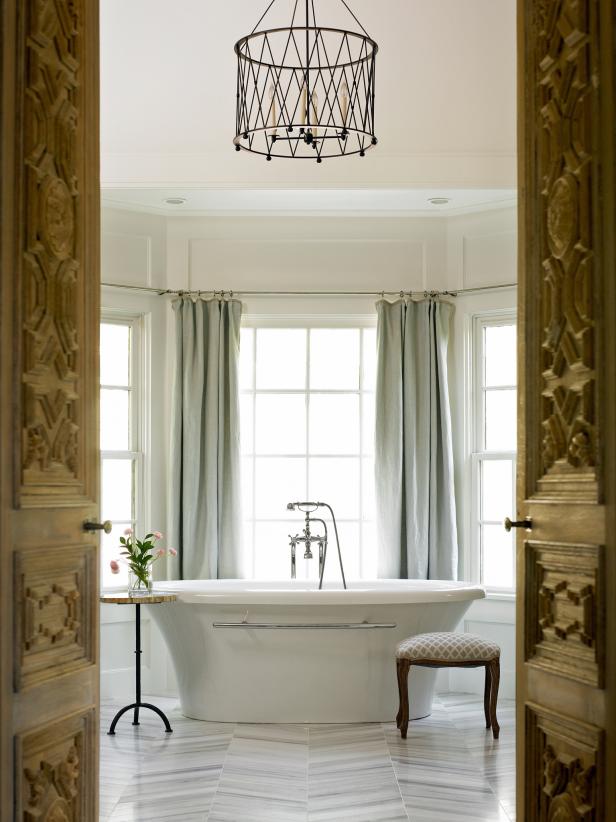 Freestanding Tub in White Spa Bathroom With Bay Window and Chandelier