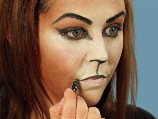 To turn yourself into an adorable cat for Halloween, cover your face with a blend of dark and light foundations to create the cat-face shape. Darken brows and create a bold cat eye with black eyeliner. Then use eyeliner to fill in just under the tip of the nose and on the inside edges of the nostrils. Then draw a line from the nose down to the lips. Fill in the point of the Cupid's bow on the lips, and then cover the top part of the upper lip with black. Extend the lip line out past the natural edge and curl up slightly. Avoid rubbing the lips together. Cover the inside of the bottom lip with nude lipstick. Use a translucent powder to set makeup in place.