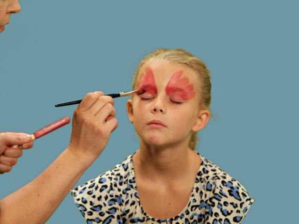 To transform your child or yourself into a beautiful butterfly for Halloween, use a wide brush to apply face paint over the eyelid and up the forehead in large strokes. Continue to make the wing strokes under the eye from the inner corner of the eye moving outward and downward. Next, use a small craft brush and orange paint to create highlights. Repeat this step using gold face paint to add more definition to each wing.