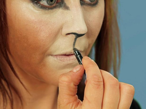 To turn yourself into an adorable cat for Halloween, cover your face with a blend of dark and light foundations to create the cat-face shape. Darken brows and create a bold cat eye with black eyeliner. Then use eyeliner to fill in just under the tip of the nose and on the inside edges of the nostrils. Then draw a line from the nose down to the lips. Fill in the point of the Cupid's bow on the lips, and then cover the top part of the upper lip with black. Extend the lip line out past the natural edge and curl up slightly. Avoid rubbing the lips together. Cover the inside of the bottom lip with nude lipstick. Use a translucent powder to set makeup in place.