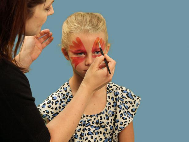 To transform your child or yourself into a beautiful butterfly for Halloween, use a wide brush to apply face paint over the eyelid and up the forehead in large strokes. Continue to make the wing strokes under the eye from the inner corner of the eye moving outward and downward. Next, use a small craft brush and orange paint to create highlights. Repeat this step using gold face paint to add more definition to each wing.