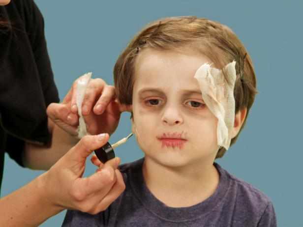 Woman applying Halloween mummy makeup to boy
