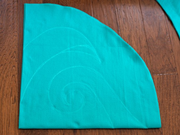 Fold turquoise felt into quarters and sketch a large, simple design in chalk onto felt. Note: This design will be cut out as the felt is still folded, creating a symmetrical design, similar to a paper snowflake.