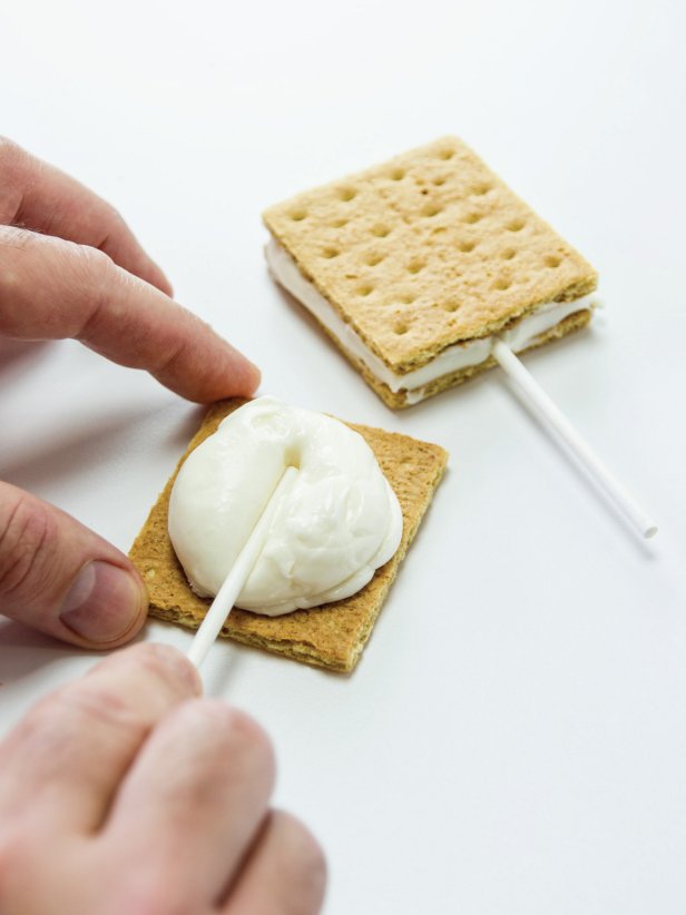 Place a lollipop stick in the middle of the marshmallow filling with the top of the stick about an inch from the bottom edge of the graham cracker.