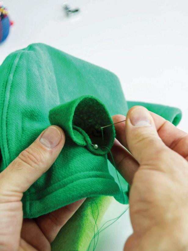 Hand sew the eye sockets in place on the top of the hoodie using a sewing needle and green thread.