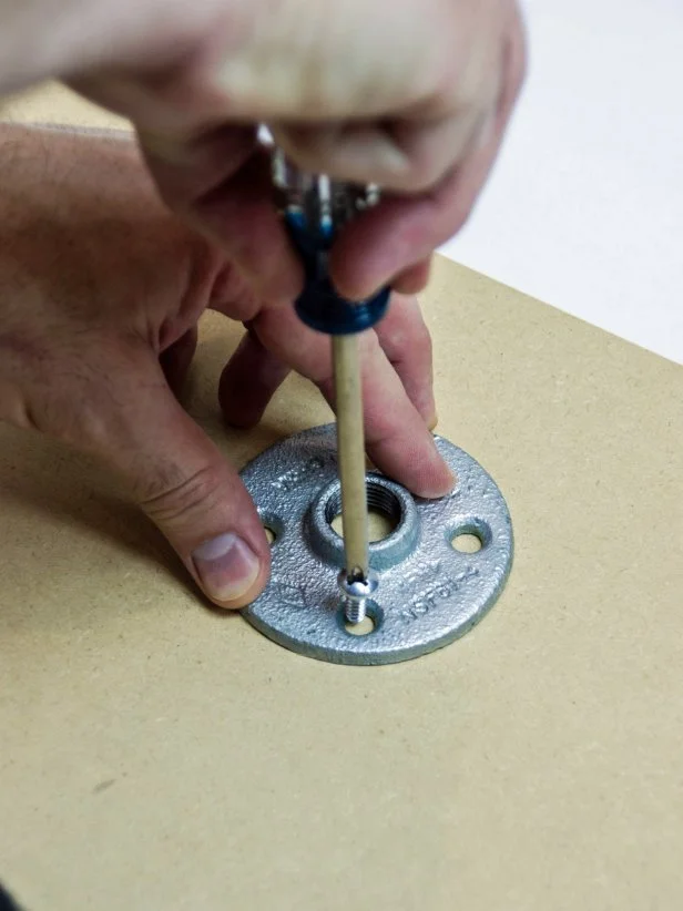 Attach the galvanized floor flange to the 15” x 15” mdf square at the spot under the right shoe and just in front of the heel using 3/4” screws.