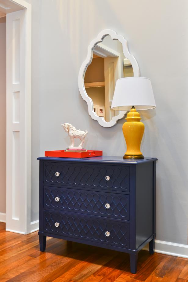 This space gets a visual charge from primary colors, including a blue dresser, red tray and yellow lamp. The mirror's white frame adds depth to the wall behind it.
