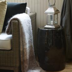 Closeup of Black Ceramic Table With Textured Bumps Beside Wicker Sofa With Fuzzy Throw Blanket and Contrasting Pillow Colors