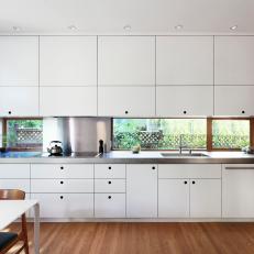 Modern White Laminate Kitchen Cabinetry Separated By a Long Window Backsplash and Stainless Steel Countertop