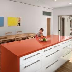 Modern Kitchen With Deep Orange Island Countertop, Long Wood Dining Table and Sliding Glass Door To Patio 