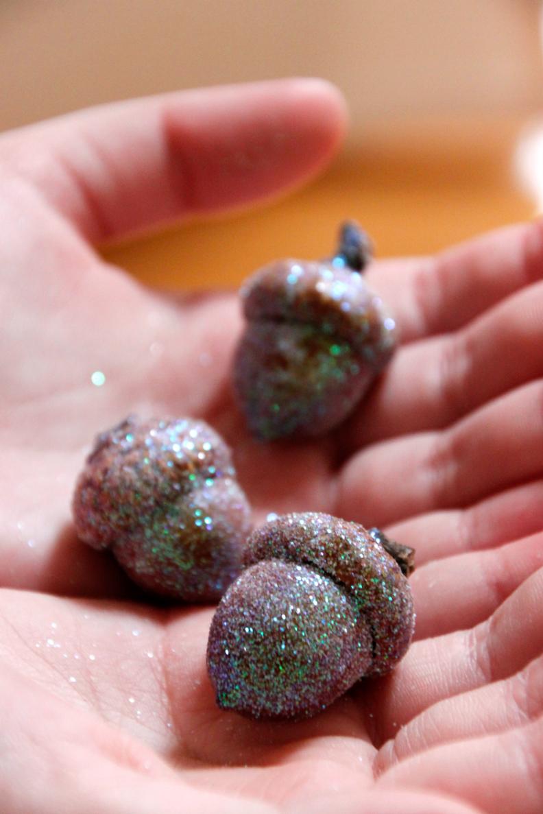 To make these glitter acorns, simply use a paint brush and coat them with mod podge. Then roll them in glitter and allow them to dry.
