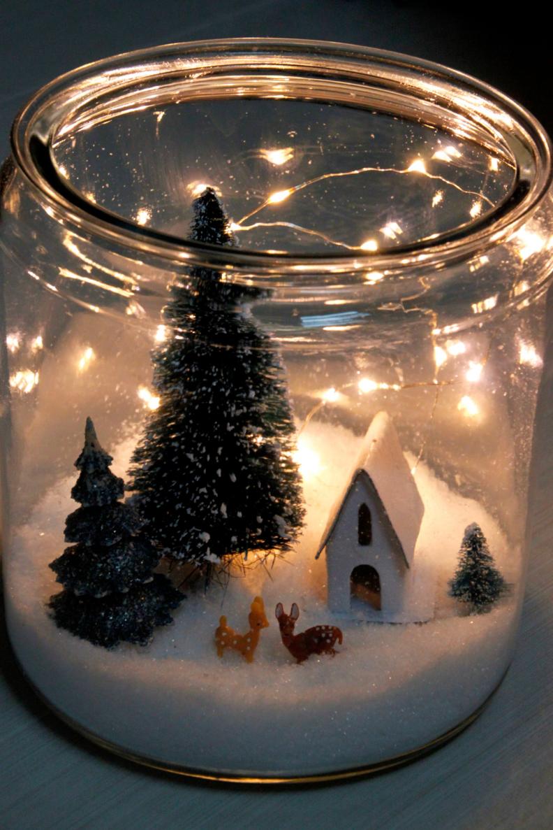 For this craft, add a layer of fake snow to the bottom of a glass container. Next add in wintry miniatures and then tuck in a set of battery powered lights to illuminate the evening sky.