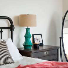 Close Up On Country Nightstand With Turquoise Lamp Base, Metal Bed Frame and Striped Throw Pillow 