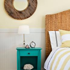 Vibrant Turquoise Bed Side Table Under Nautical Wood-Framed Mirror in Coastal Bedroom With Wicker Headboard 