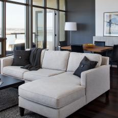 Stylish Modern Living Room With Window Wall, Neutral Sectional, Charcoal Gray Accent Wall Panel and Connected Dining Room