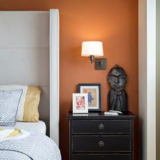 Asian Bed Side Table With Themed Decor in Front of Orange Painted Accent Wall in Bedroom 