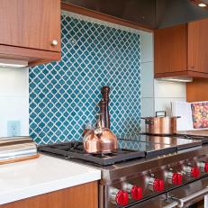 Close Up on Decorative Blue Tile Accent Over Stainless Steel Stove With Cherry Red Knobs and Copper Pots 