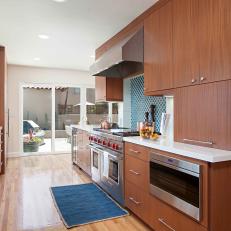Long Midcentury Modern Kitchen With Sleek Woodgrain Cabinetry, Stainless Steel Appliances and White Countertop 