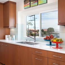 Ample Woodgrain Cabinetry Framing Sliding Window, White Countertop and Colorful Fruit Display 