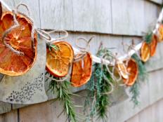 A garland with dried citrus, herbs, and greenery is hung on a wall.