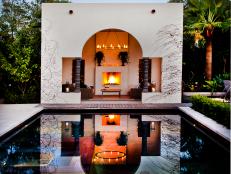 A courtyard fireplace is reflected in the swimming pool before it