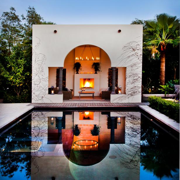 A courtyard fireplace is reflected in the swimming pool before it