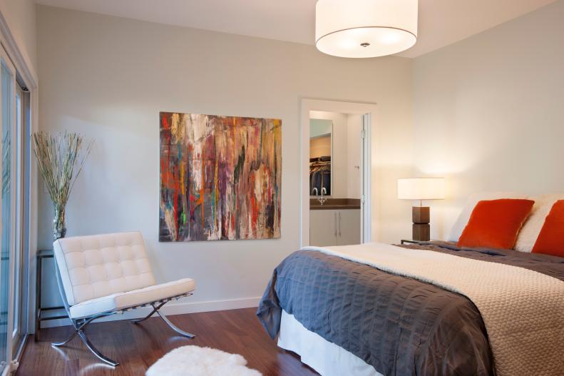 Neutral Modern Bedroom With White Chair, Gray Bedding & Orange Pillows