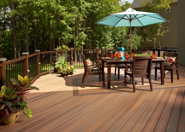 This composite deck from Fiberon features a darker inlay pattern that defines the outdoor dining area, the same way an outdoor rug would. Accessories provide pops of color to contrast the Fiberon Horizon Dark Walnut composite railing, matching post-sleeve lighting and round black balusters.