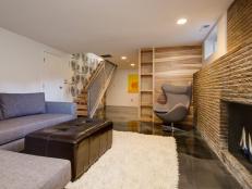 White Basement With Gray Sectional, Leather Ottoman & Fireplace
