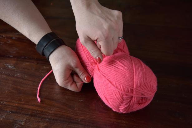 Use this strand to cinch the center of the skein by pulling it tight and knotting it, creating the look of two equal halves. Once the ends of the wound up yarn are cut, one half will become the solid ball and the other half will become the loose yarn strands that will create the pom-pom look.