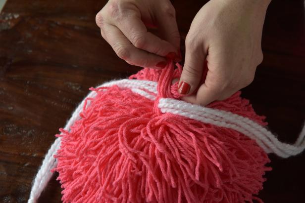 Cut a 10-inch strand of yarn in a contrasting color to size with scissors, then loop it through the top of the pom-pom, knot and secure. This will be used to tie the pom-pom in place.