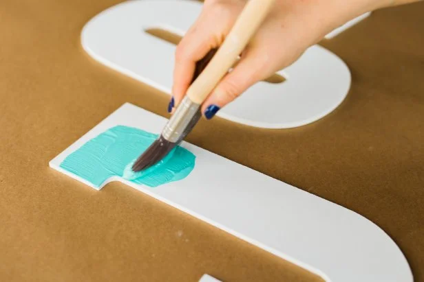 Use the paint brush to coat the front of the letters. TIP: Since chipboard tends to soak up paint quickly, you’ll need at least two coats of paint for every letter to ensure proper coverage.