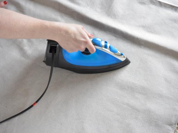 On a flat, level surface, use the iron set on the steam function to remove all wrinkles from the drop cloth.