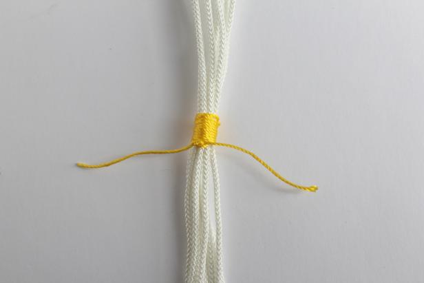 Gather all 8 strands and tie a piece of the yellow rope around them all. Wrap the yellow rope around the white ropes, creating a stripe. This is the same technique as step #3.