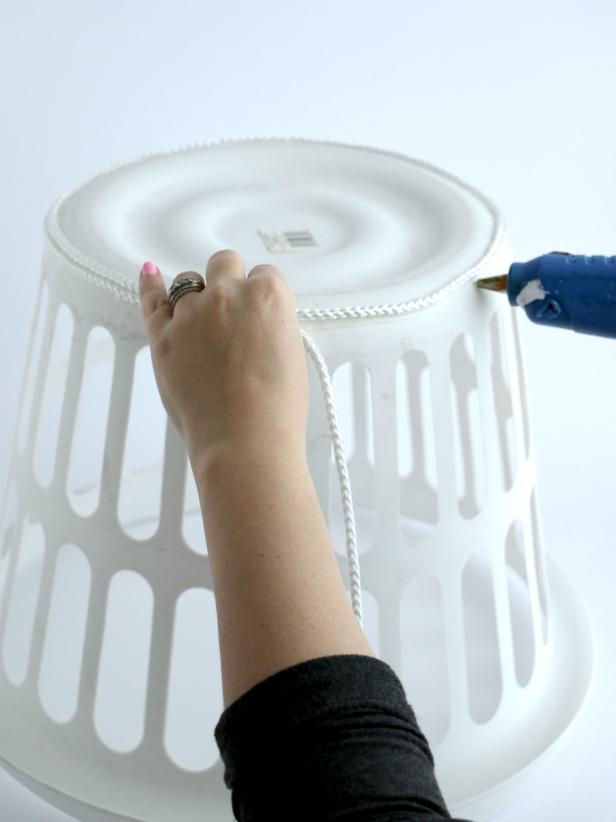 Start wrapping the white rope around the basket by placing strips of hot glue and then pushing the rope into the glue.