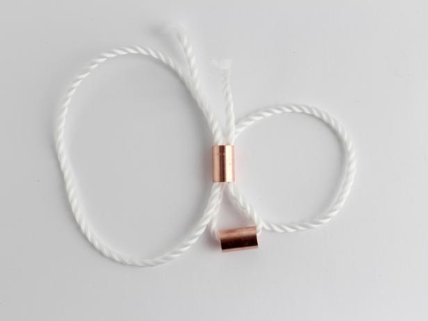Take each rope end and thread it back up the copper piece, creating two loops on each side.