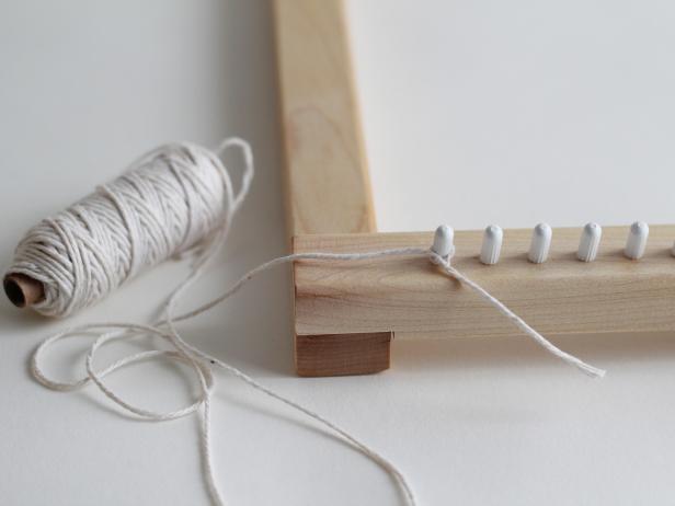 The weaving will be made of yarn that goes vertically, called the warp, and horizontally, called the weft. The first step is to create the warp on your loom with the thin, white cotton yarn. On the very left bottom peg, tie on the yarn. String the yarn up to the left top peg, around, and back down.