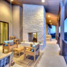 Contemporary Covered Porch With Wood Furniture and Tall Stone Fireplace 