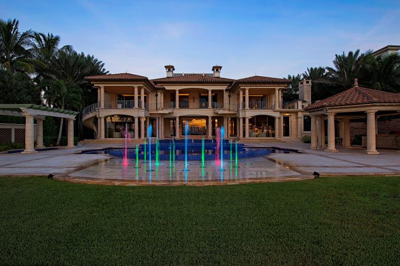 Back Exterior of Mediterranean Home With Pool and Lighted Fountains