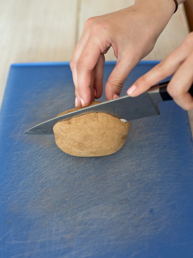 Using a sharp knife cut a large white potato in half.