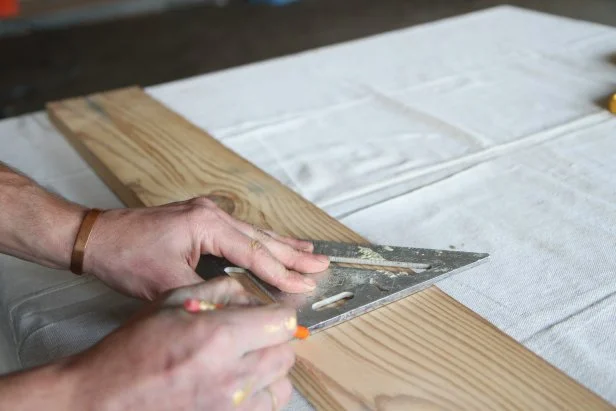 Use a speed square to make a straight line on a wood plank.