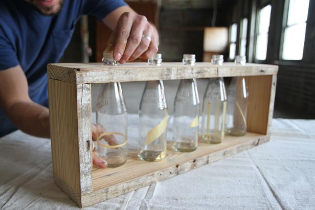 Dan Faires placing glass bottles inside a wood centerpiece