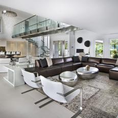Open Modern Living Room With Brown Leather Sectional, Silver Bean Shaped Coffee Tables and Modern White Chairs 