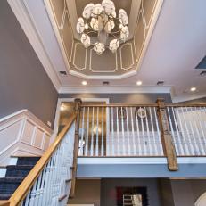 Mid-Staircase View of Second Floor and the Gray Tray Ceiling With White Frame Design and Lampshade Chandelier  