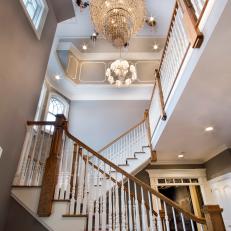 Upward View of Foyer Crystal Chandelier Over Turning Staircase With Wood Columns and Gray Walls