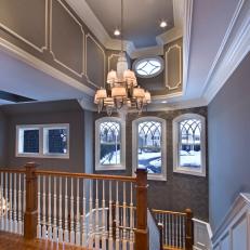 Second Story View of Open Staircase With Charcoal Wallpaper Accent Wall and Deep Tray Ceiling With Lampshade Chandelier 